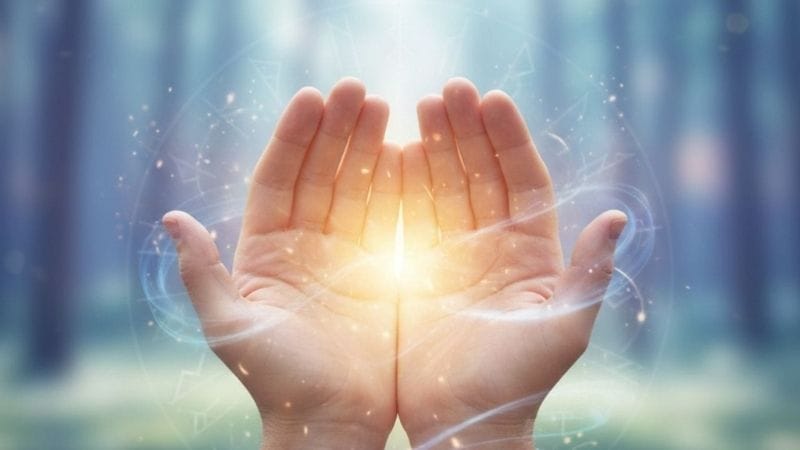 Mãos transmitindo energia de cura com luz azul e branca ao redor.